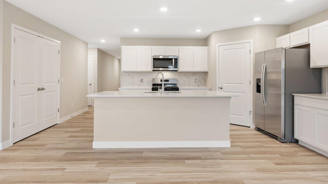 fawn creek estates freeport - kitchen with white cabinets, quartz countertops, tile backsplash, corner pantry, stainless steel appliances, lvp flooring, and island with seating