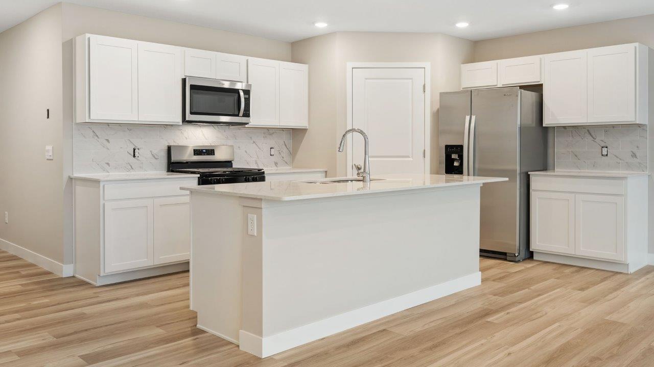 fawn creek estates freeport - kitchen with white cabinets, quartz countertops, tile backsplash, corner pantry, stainless steel appliances, lvp flooring, and island with seating