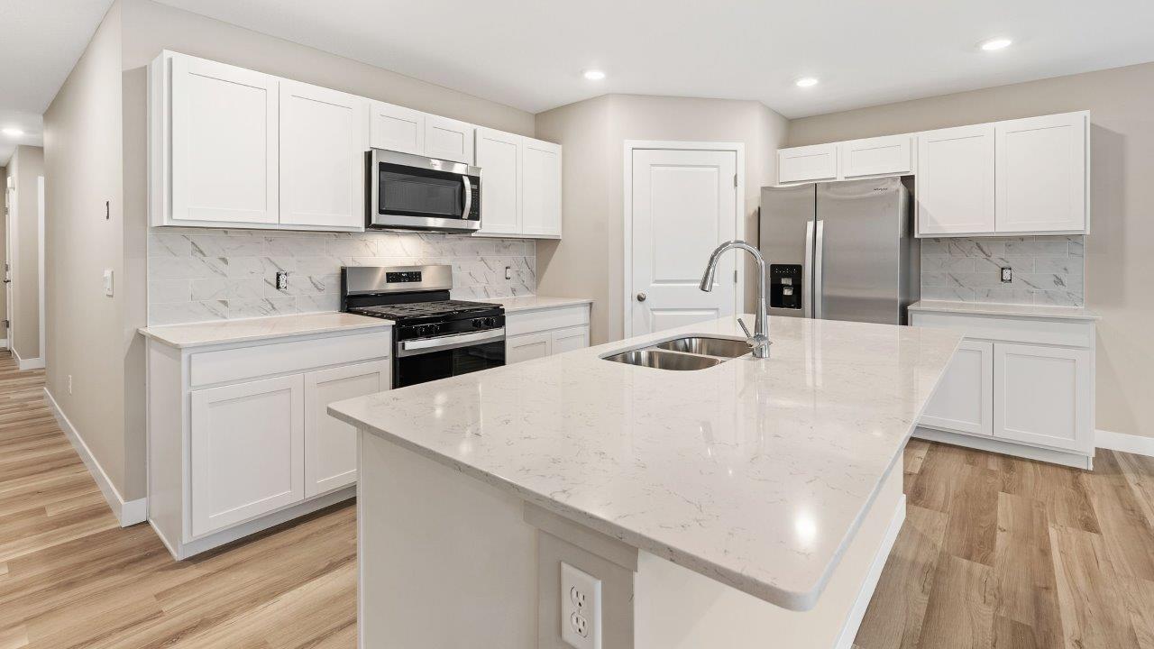 fawn creek estates freeport - kitchen with white cabinets, quartz countertops, tile backsplash, corner pantry, stainless steel appliances, lvp flooring, and island with seating
