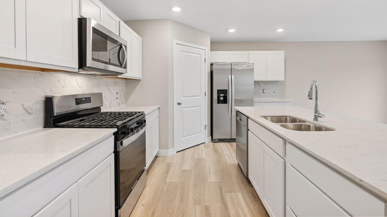 fawn creek estates freeport - kitchen with white cabinets, quartz countertops, tile backsplash, corner pantry, stainless steel appliances, lvp flooring, and island with seating