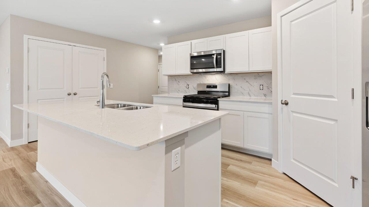 fawn creek estates freeport - kitchen with white cabinets, quartz countertops, tile backsplash, corner pantry, stainless steel appliances, lvp flooring, and island with seating