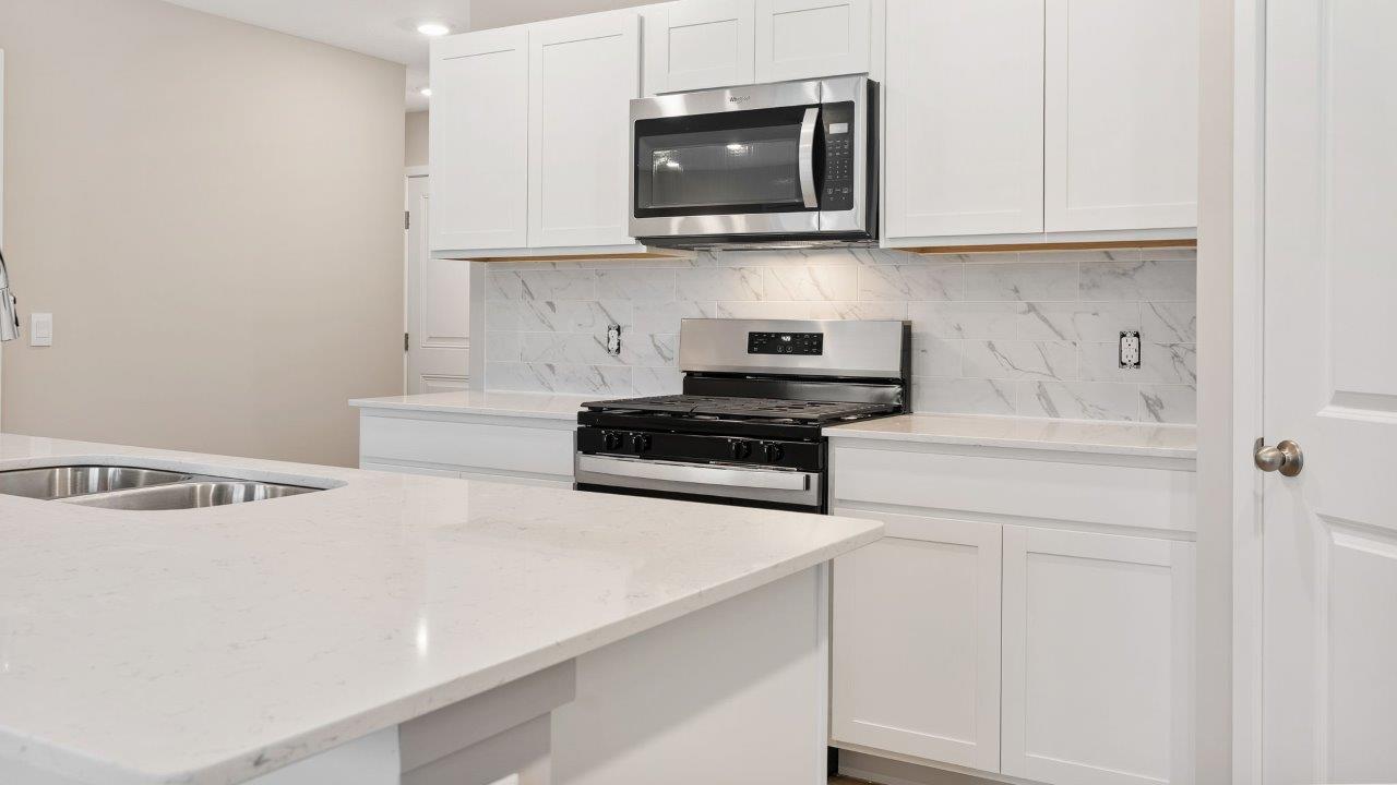 fawn creek estates freeport - kitchen with white cabinets, quartz countertops, tile backsplash, corner pantry, stainless steel appliances, lvp flooring, and island with seating