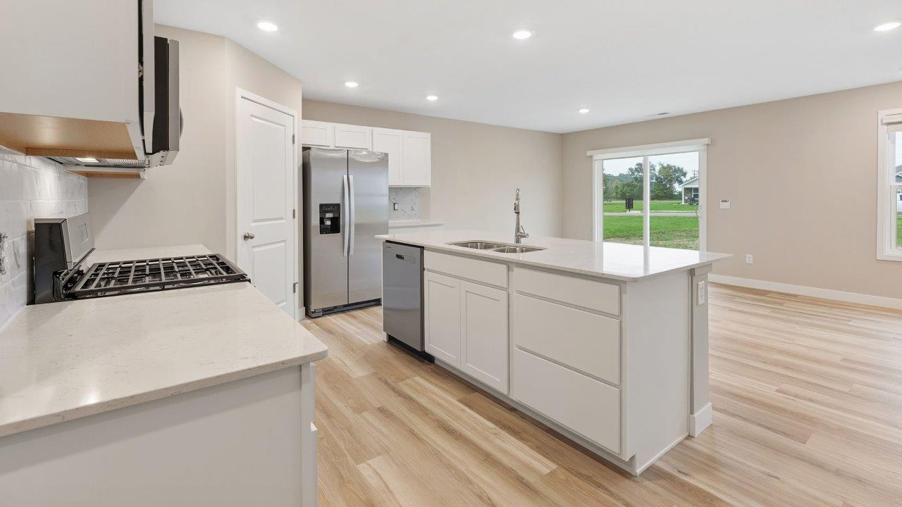 fawn creek estates freeport - kitchen with white cabinets, quartz countertops, tile backsplash, corner pantry, stainless steel appliances, lvp flooring, and island with seating