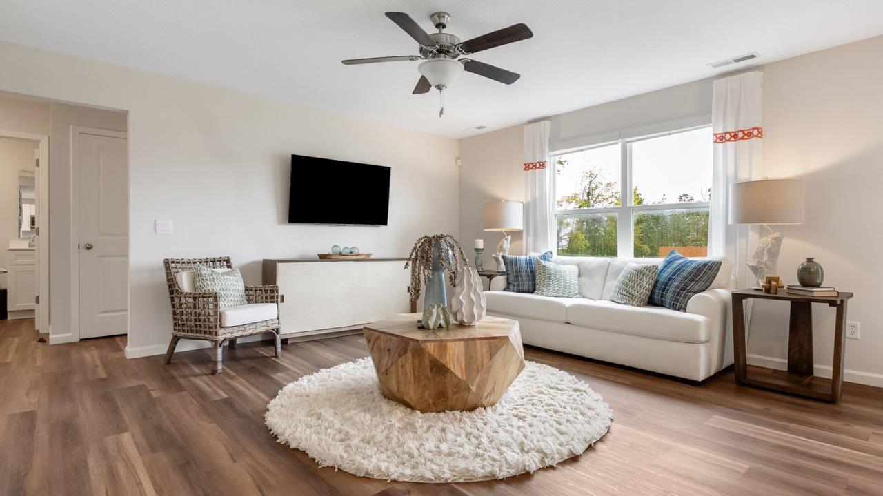 farmstead at carroll creek henley model home open layout living room with mohawk eastmont lvp, ceiling fan, 2 windows, and heron plume painted walls