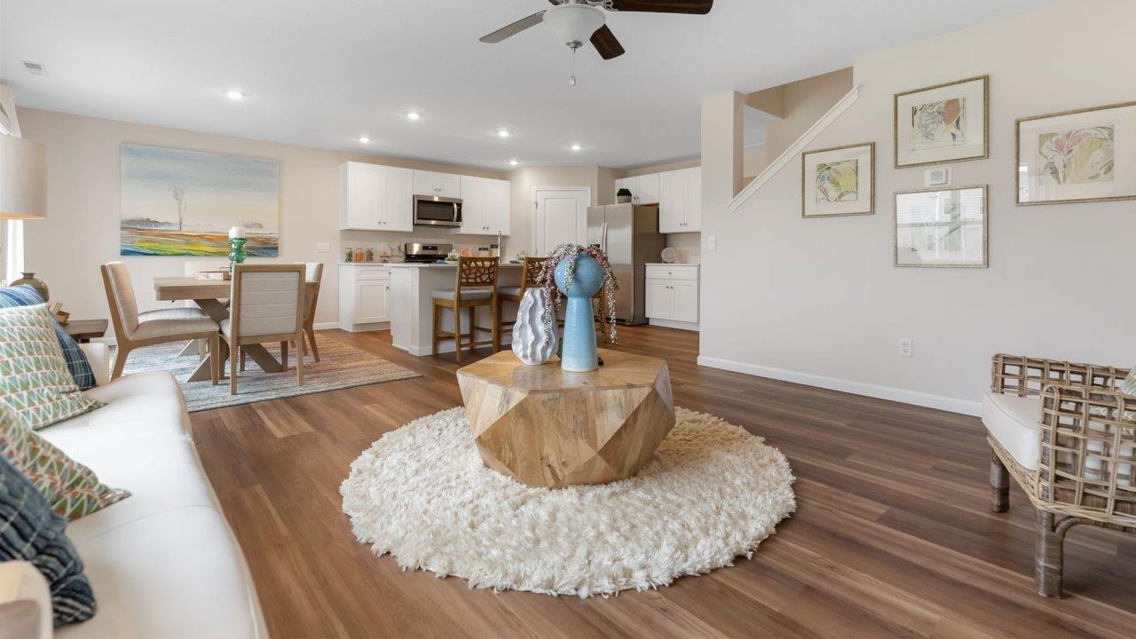 farmstead at carroll creek henley model home open layout living room with mohawk eastmont lvp, ceiling fan, 2 windows, and heron plume painted walls