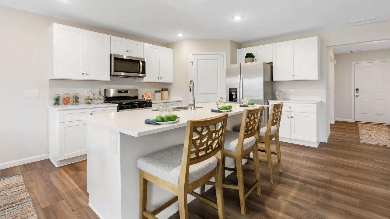 farmstead at carroll creek henley model home kitchen with white shaker cabinets, island with seating, pantry, stainless steel appliances, and quartz countertops
