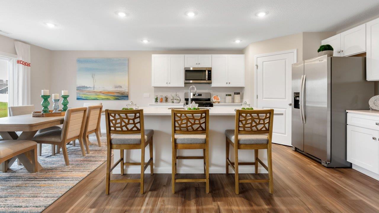 farmstead at carroll creek henley model home kitchen with white shaker cabinets, island with seating, pantry, stainless steel appliances, and quartz countertops