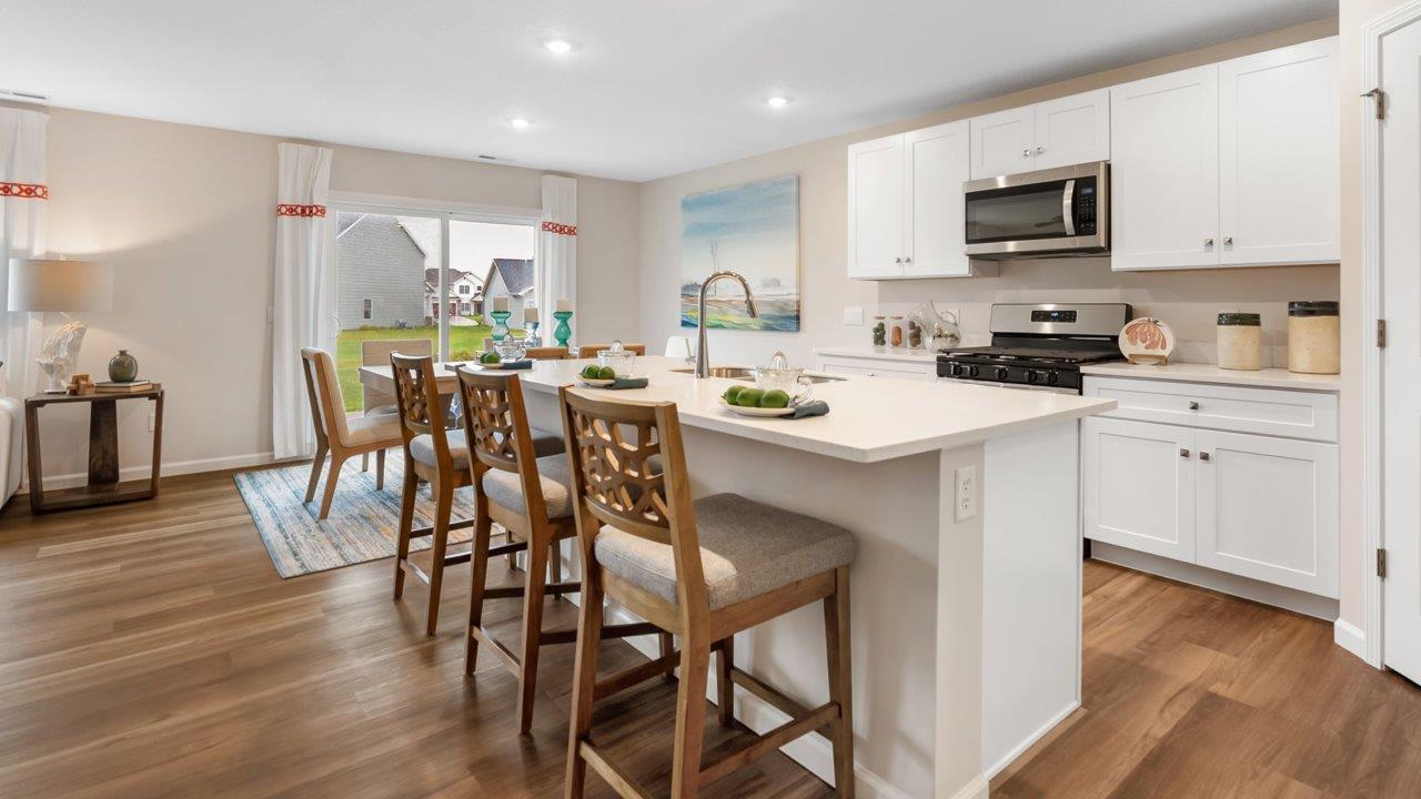 farmstead at carroll creek henley model home kitchen with white shaker cabinets, island with seating, pantry, stainless steel appliances, and quartz countertops