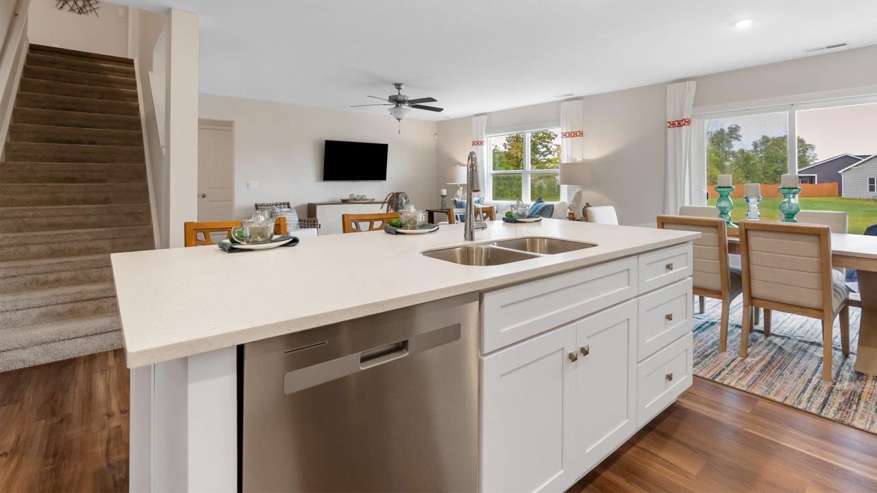 farmstead at carroll creek henley model home kitchen with white shaker cabinets, island with seating, pantry, stainless steel appliances, and quartz countertops