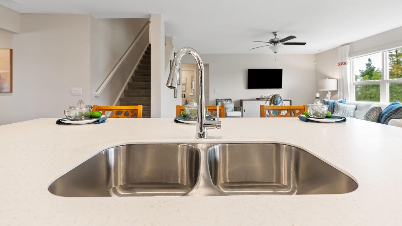 farmstead at carroll creek henley model home kitchen with white shaker cabinets, island with seating, pantry, stainless steel appliances, and quartz countertops