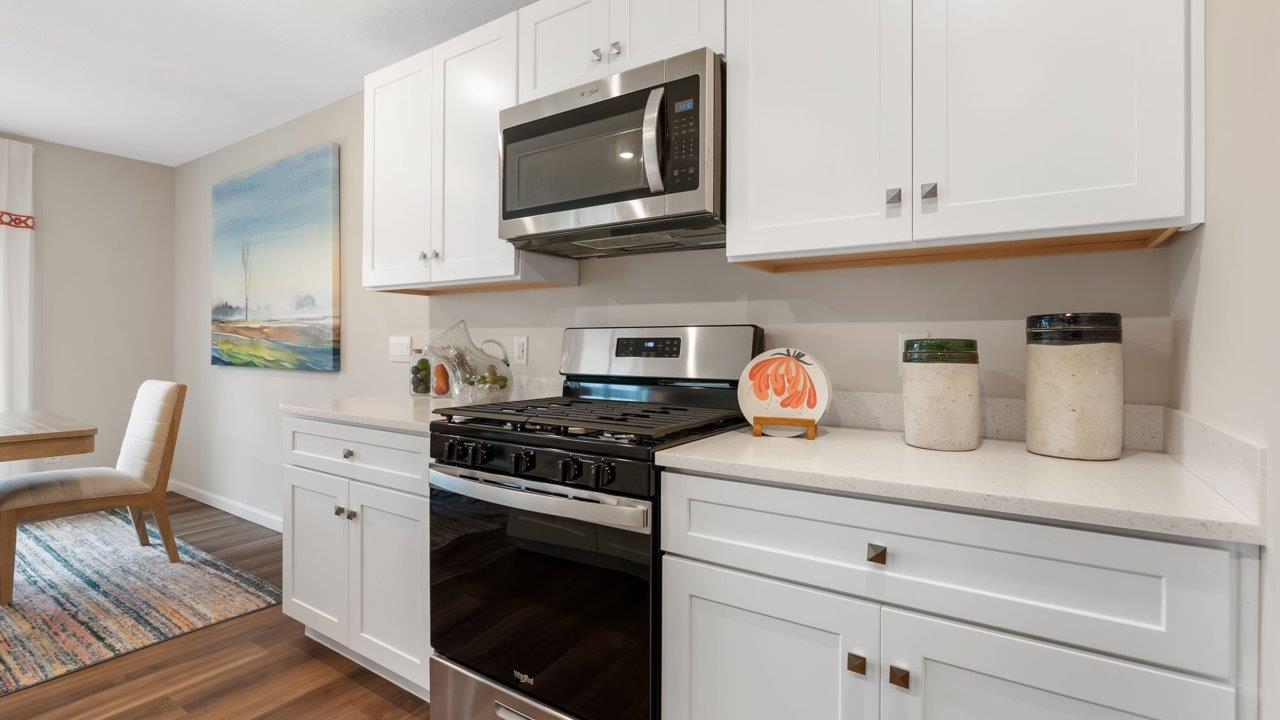 farmstead at carroll creek henley model home kitchen with white shaker cabinets, island with seating, pantry, stainless steel appliances, and quartz countertops