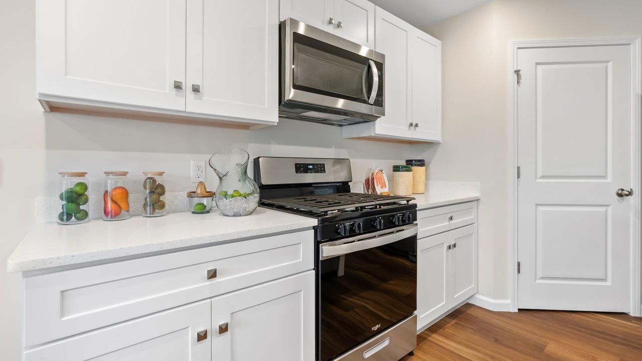 farmstead at carroll creek henley model home kitchen with white shaker cabinets, island with seating, pantry, stainless steel appliances, and quartz countertops