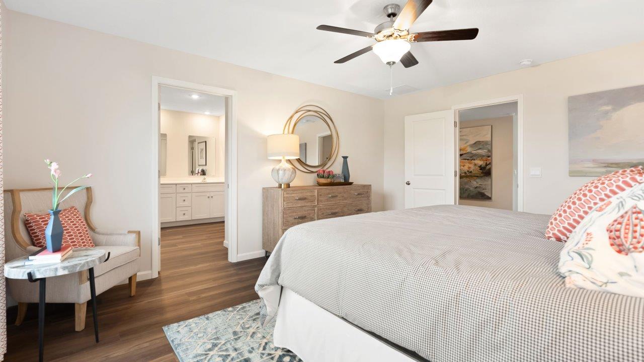 farmstead at carroll creek henley model home primary bedroom with mohawk lvp flooring, 2 windows, ceiling fan, heron plume painted walls, and ensuite walk in closet and bathroom
