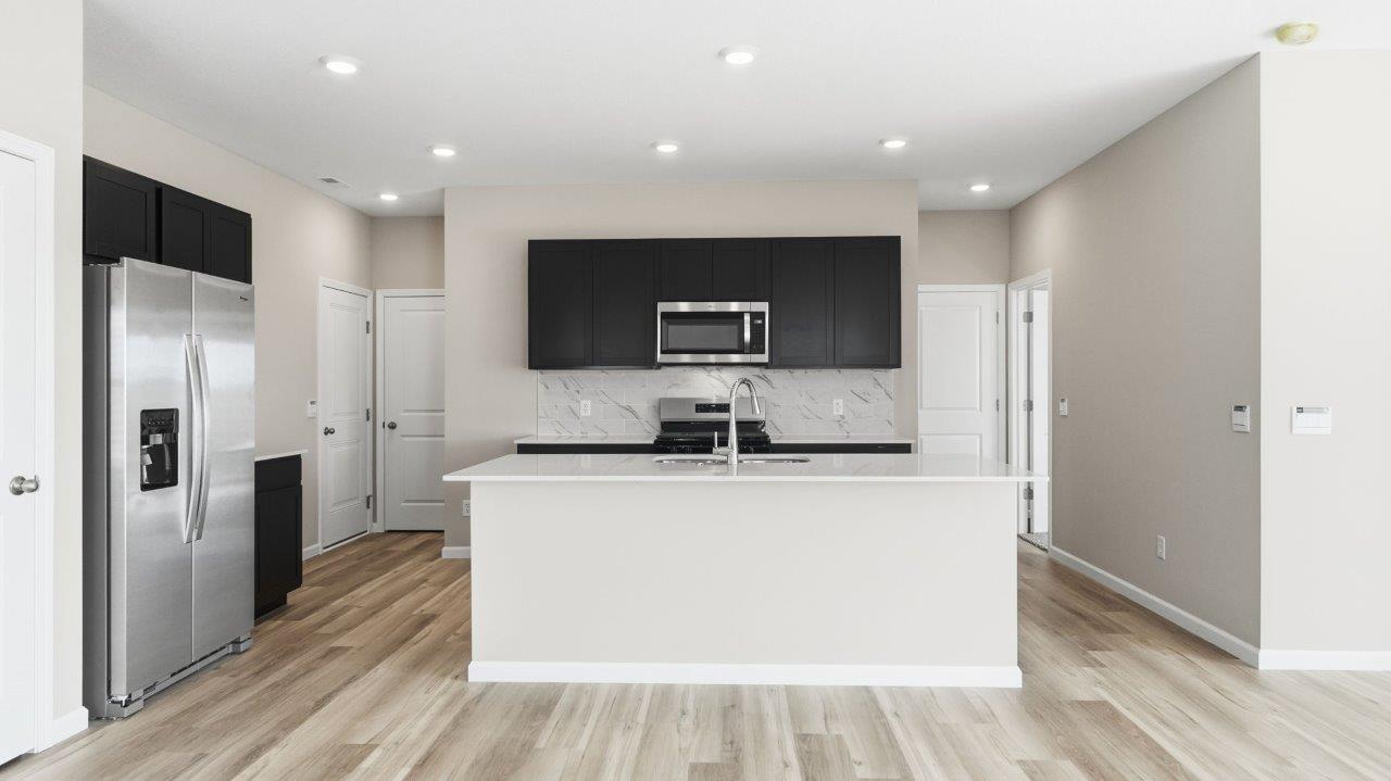 sonora elm kitchen with sarsaparilla cabinets, stainless steel appliances, center island with bar seating, quartz countertops, tile backsplash, and lvp flooring
