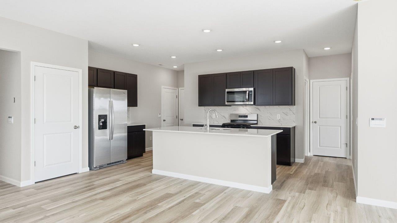 sonora elm kitchen with sarsaparilla cabinets, stainless steel appliances, center island with bar seating, quartz countertops, tile backsplash, and lvp flooring