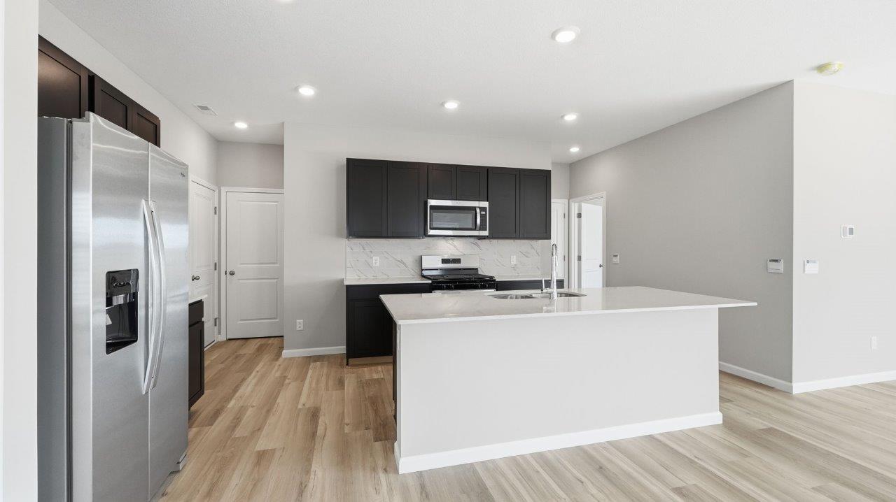 sonora elm kitchen with sarsaparilla cabinets, stainless steel appliances, center island with bar seating, quartz countertops, tile backsplash, and lvp flooring