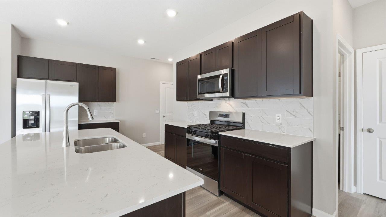 sonora elm kitchen with sarsaparilla cabinets, stainless steel appliances, center island with bar seating, quartz countertops, tile backsplash, and lvp flooring