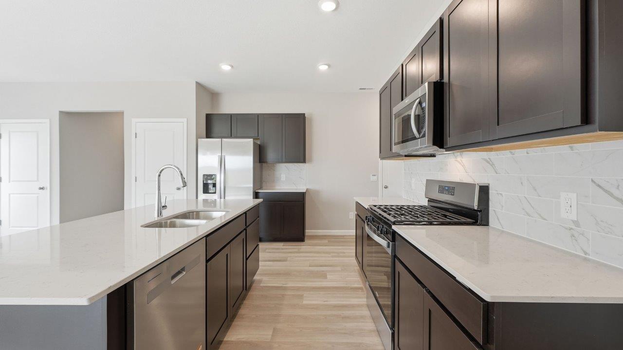 sonora elm kitchen with sarsaparilla cabinets, stainless steel appliances, center island with bar seating, quartz countertops, tile backsplash, and lvp flooring