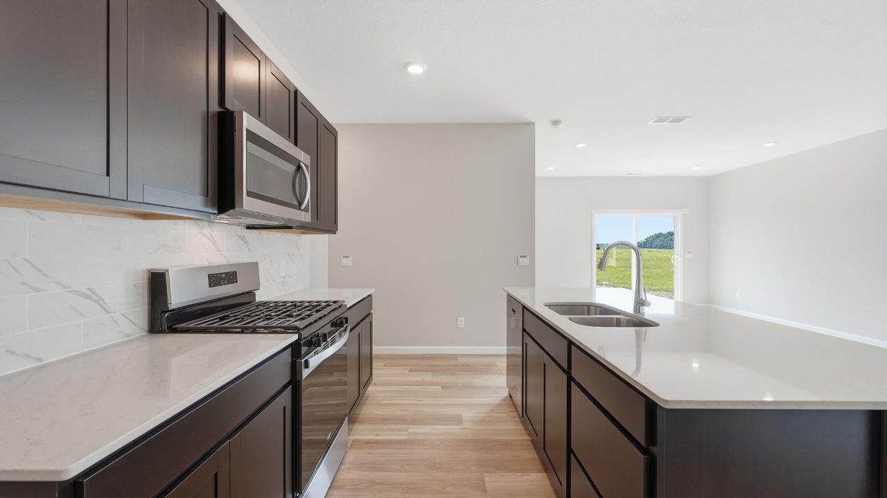 sonora elm kitchen with sarsaparilla cabinets, stainless steel appliances, center island with bar seating, quartz countertops, tile backsplash, and lvp flooring
