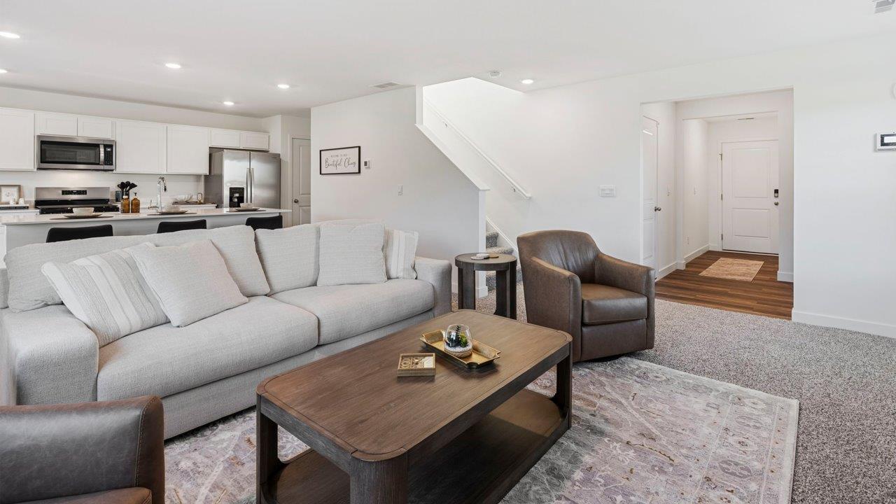 Greenbrier Pine Model Home - open layout living room with elk beige carpet flooring, white walls, and open to kitchen and casual dining spaces