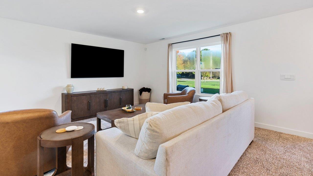 Greenbrier Pine Model Home - open layout living room with elk beige carpet flooring, white walls, and open to kitchen and casual dining spaces