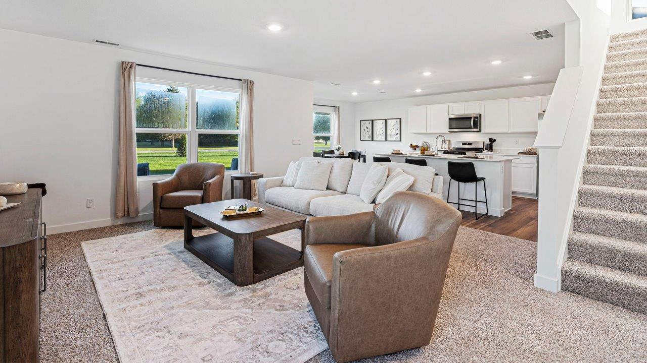 Greenbrier Pine Model Home - open layout living room with elk beige carpet flooring, white walls, and open to kitchen and casual dining spaces