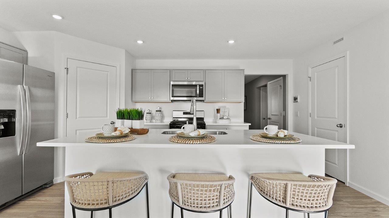 chatham kitchen with grey cabinets, quartz counters, pantry, appliances, and center island with bar seating
