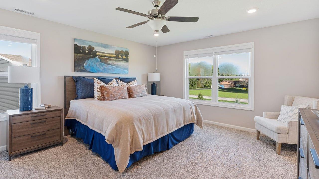 Greenbrier Stamford Model Home - primary bedroom with carpet flooring, 2 windows, ceiling fan, with ensuite bathroom and closet