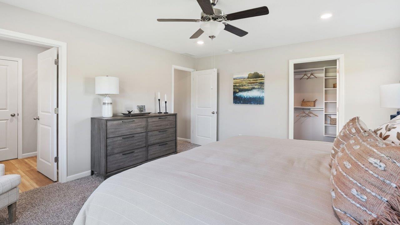 Greenbrier Stamford Model Home - primary bedroom with carpet flooring, 2 windows, ceiling fan, with ensuite bathroom and closet