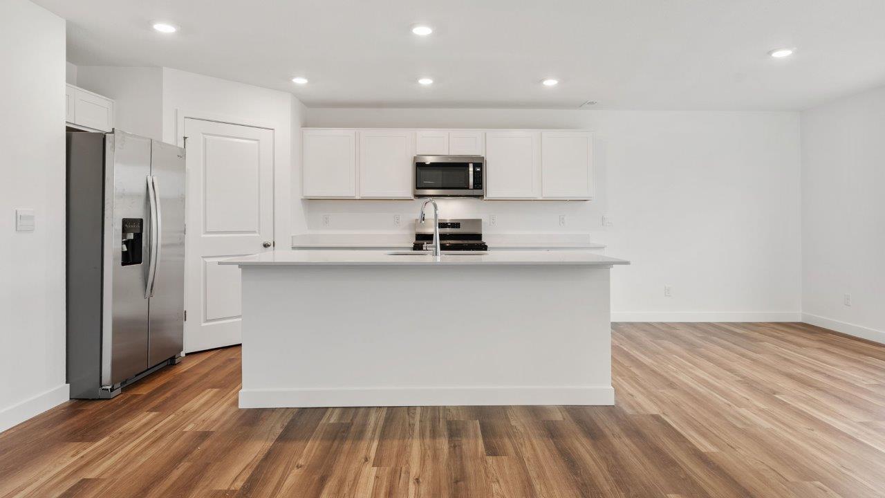 greenbrier cabral kitchen with white cabinets, stainless steel appliances, corner pantry, island with seating, and quartz countertops