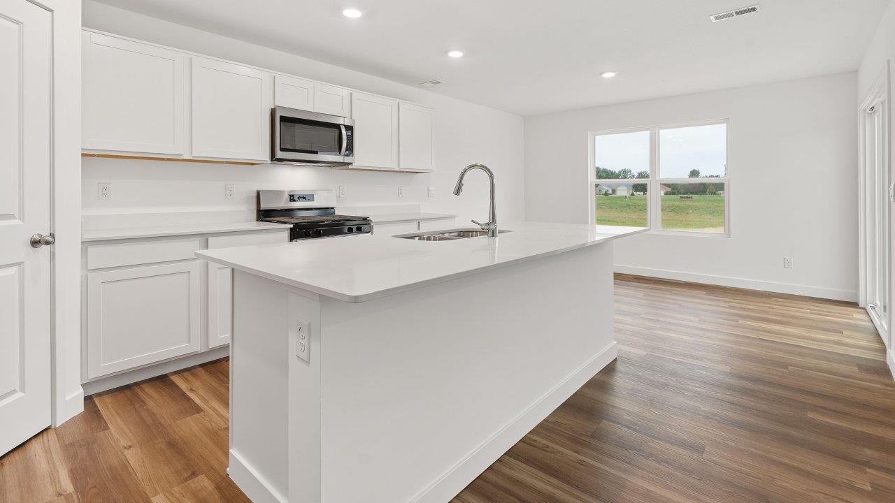 greenbrier cabral kitchen with white cabinets, stainless steel appliances, corner pantry, island with seating, and quartz countertops