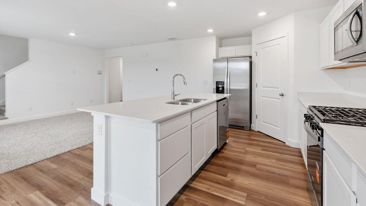 greenbrier cabral kitchen with white cabinets, stainless steel appliances, corner pantry, island with seating, and quartz countertops