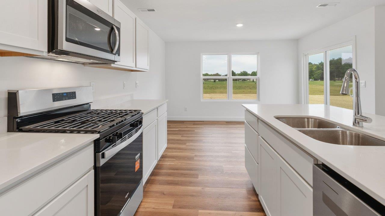 greenbrier cabral kitchen with white cabinets, stainless steel appliances, corner pantry, island with seating, and quartz countertops