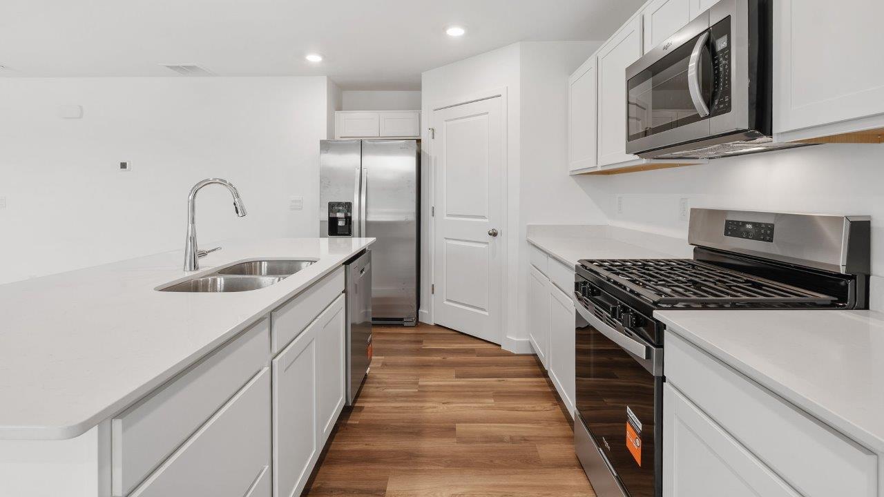 greenbrier cabral kitchen with white cabinets, stainless steel appliances, corner pantry, island with seating, and quartz countertops