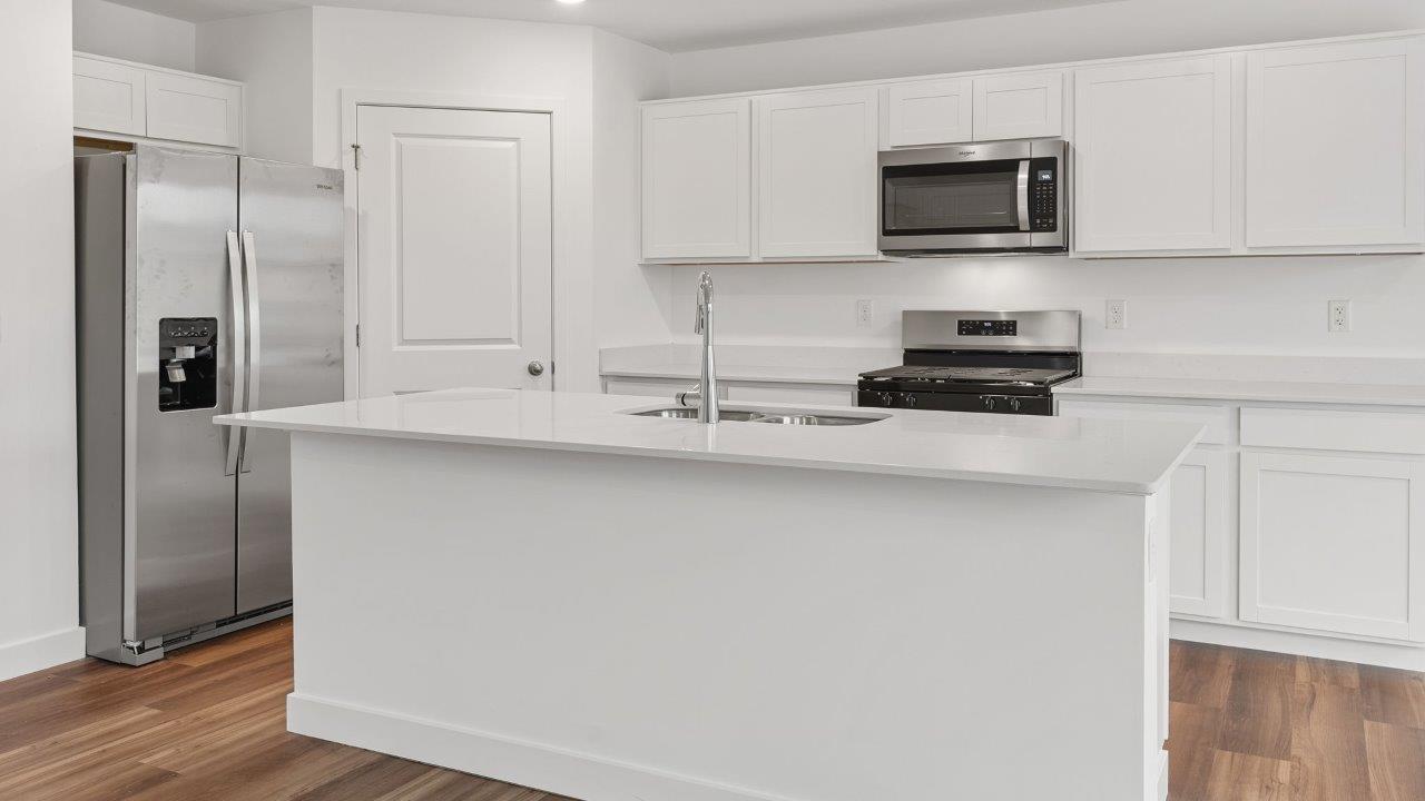 greenbrier cabral kitchen with white cabinets, stainless steel appliances, corner pantry, island with seating, and quartz countertops