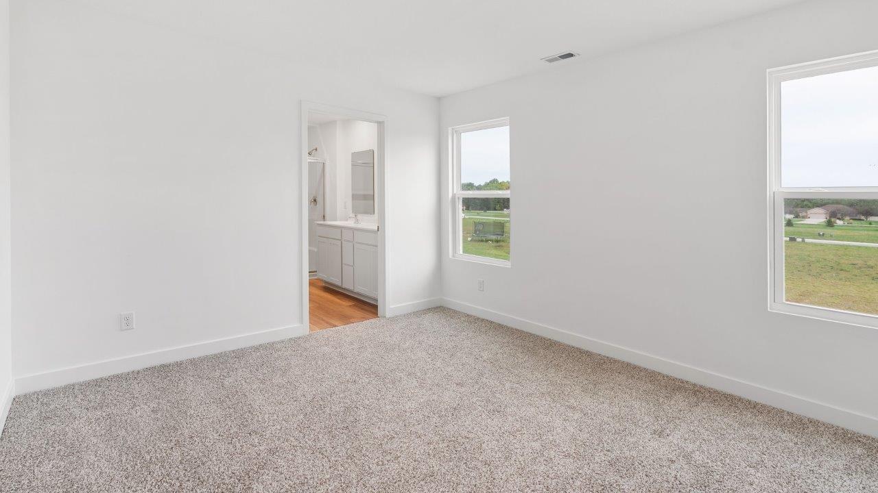 greenbrier cabral primary bedroom with ensuite bathroom and walk in closet with elk biege carpet flooring, 2 windows, and white walls