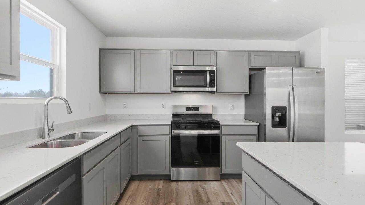 kitchen with grey cabinets, stainless steel appliances, quartz coutners, and large center island