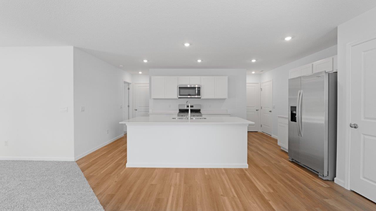 Elm kitchen with lvp flooring, white cabinets, quartz counters, appliances, and center island with bar seating