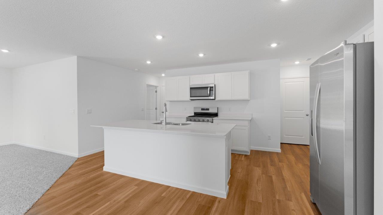 Elm kitchen with lvp flooring, white cabinets, quartz counters, appliances, and center island with bar seating