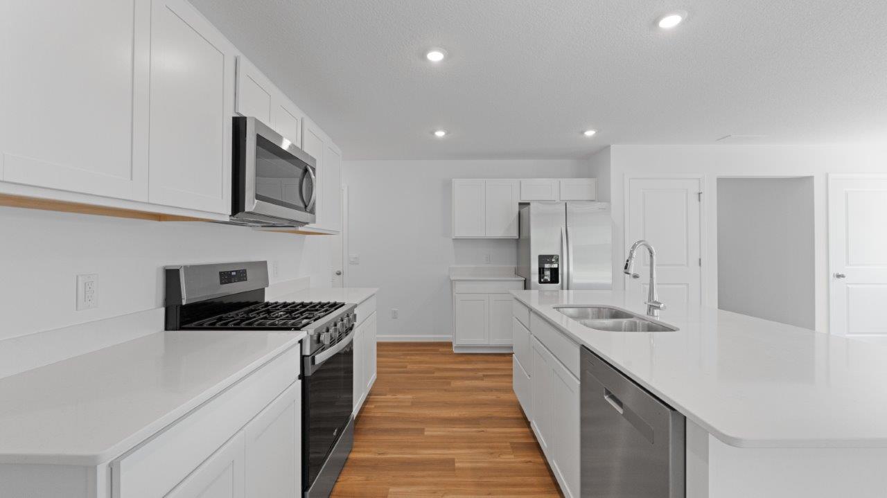 Elm kitchen with lvp flooring, white cabinets, quartz counters, appliances, and center island with bar seating