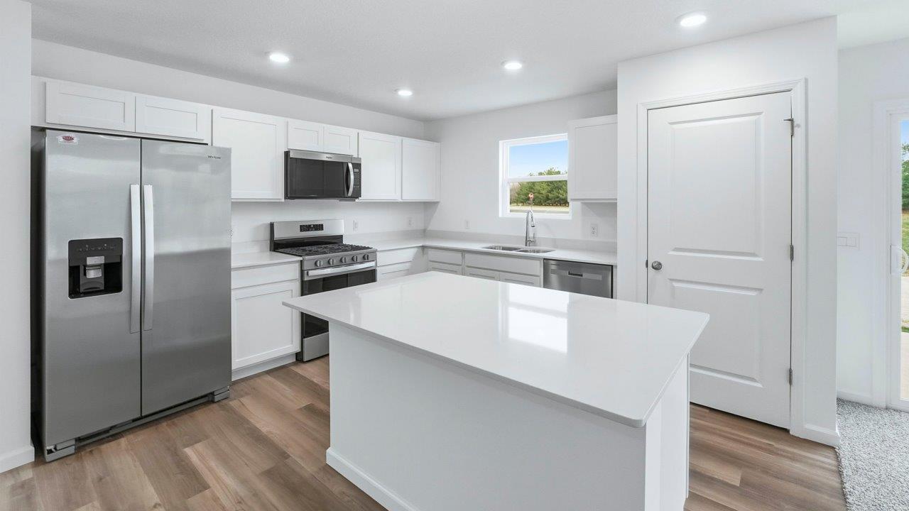 kitchen with white cabinets, quartz countertops, stainless steel appliances, center island, with lvp flooring