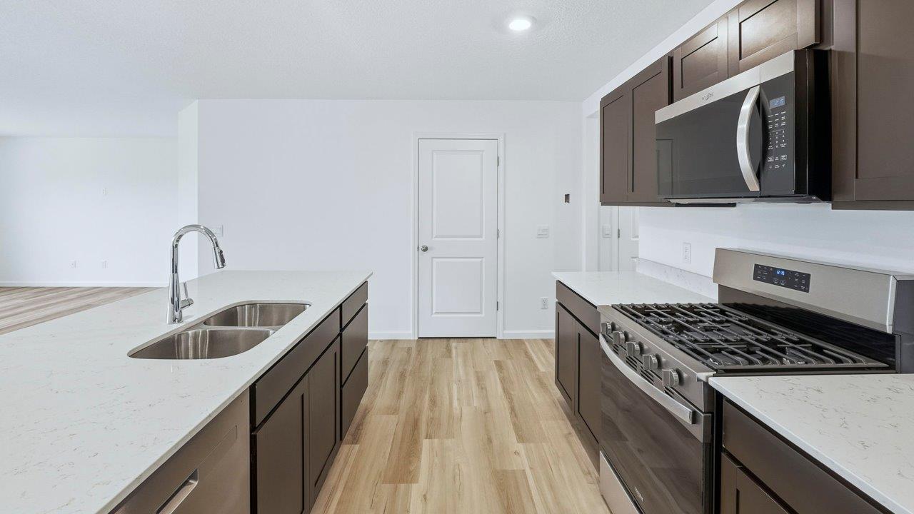 kitchen with sarsaparilla cabinets, quartz countertops, stainless steel appliances, corner pantry, center island, with lvp