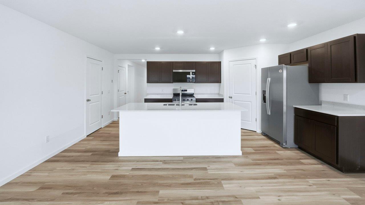 kitchen with sarsaparilla cabinets, quartz countertops, stainless steel appliances, corner pantry, center island, with lvp