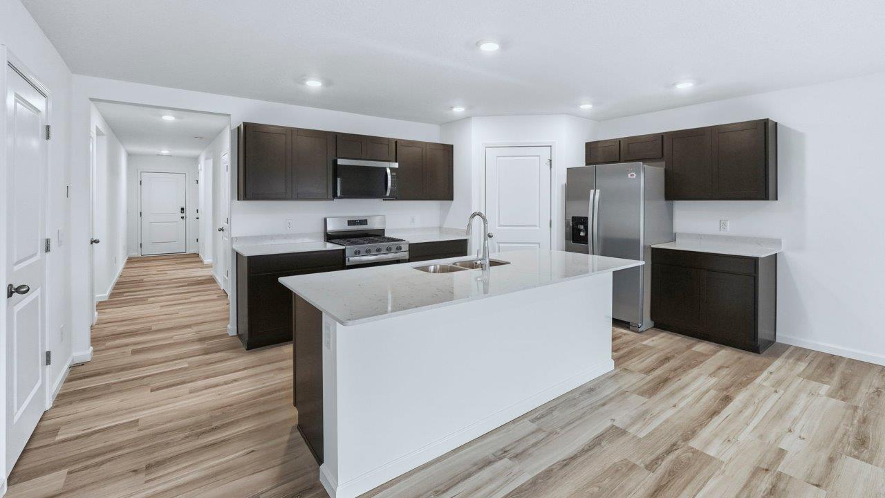 kitchen with sarsaparilla cabinets, quartz countertops, stainless steel appliances, corner pantry, center island, with lvp