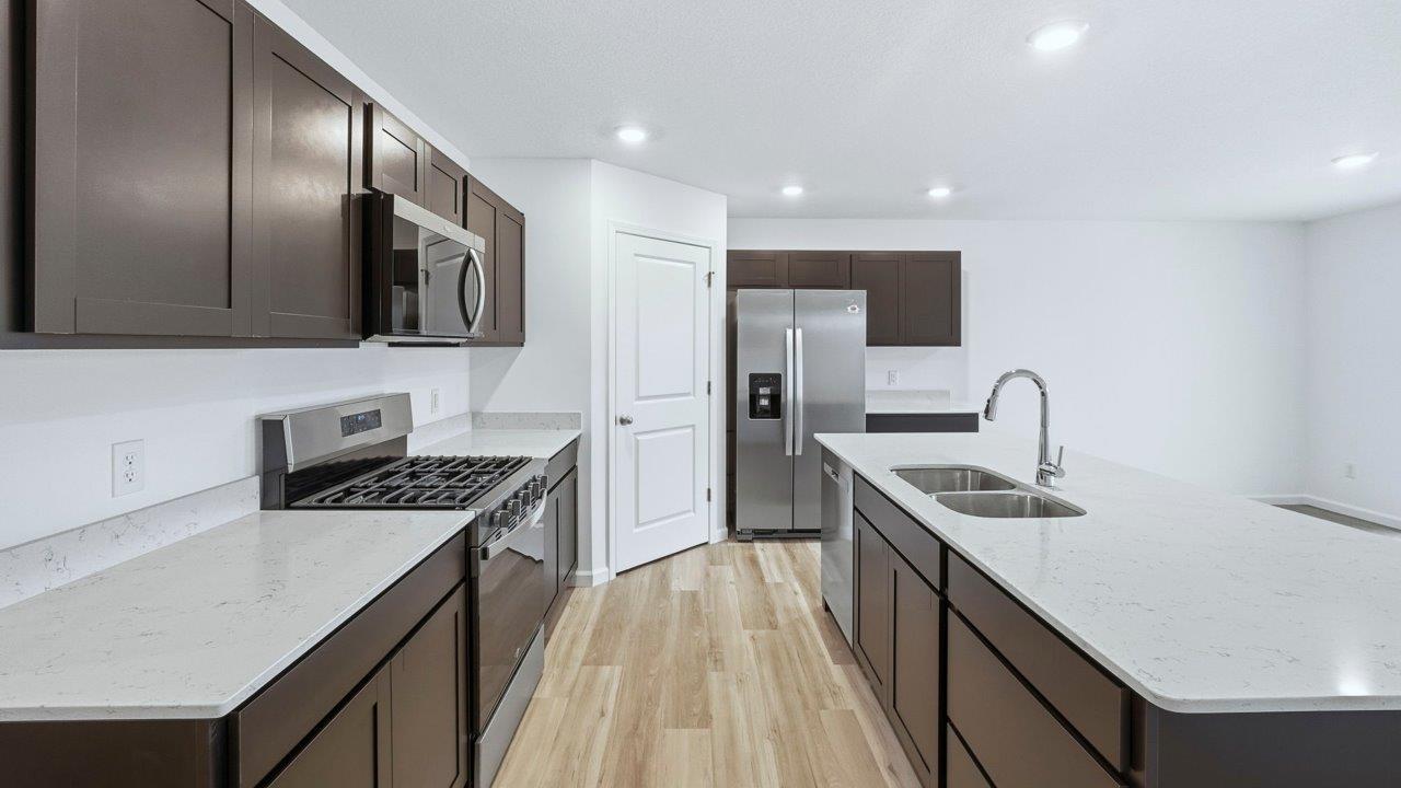 kitchen with sarsaparilla cabinets, quartz countertops, stainless steel appliances, corner pantry, center island, with lvp