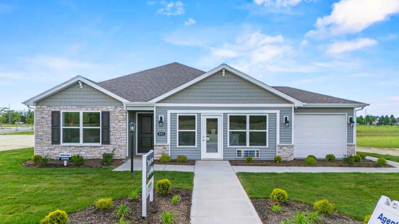 riverwalk aldridge model home exterior with 3 car garage, sodded and landscaped yard, sage vinyl siding, sage shake, chocolate shutters, and chiseled edge colorado stone