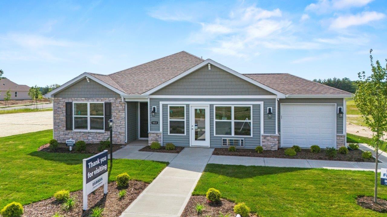 riverwalk aldridge model home exterior with 3 car garage, sodded and landscaped yard, sage vinyl siding, sage shake, chocolate shutters, and chiseled edge colorado stone