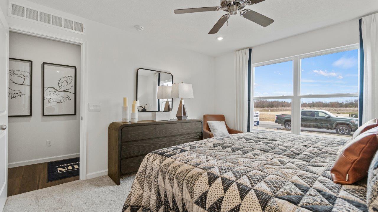 riverwalk aldridge model primary bedroom with ceiling fan, 2 windows, elk beige carpet, and ensuite bathroom and walk in closet