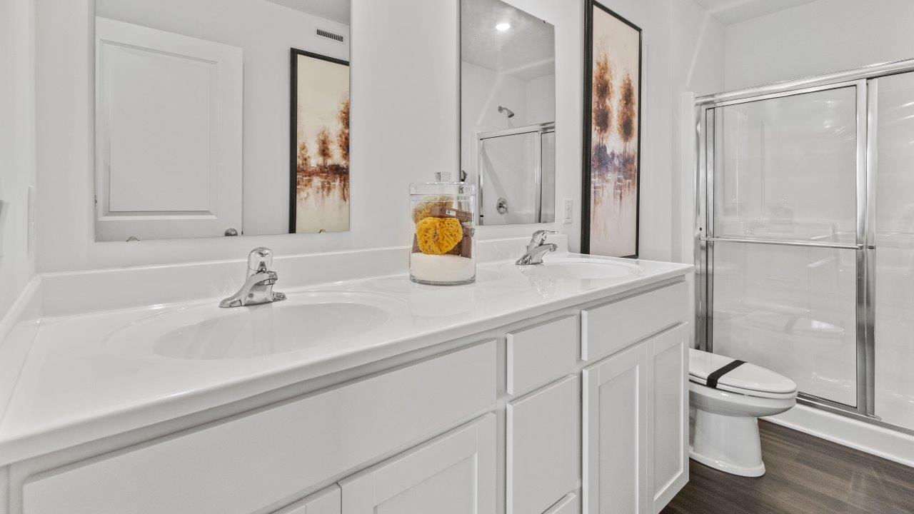 riverwalk aldridge model primary bedroom ensuite bathroom with dual sink vanity, white cabinets, and walk in fiberglass shower