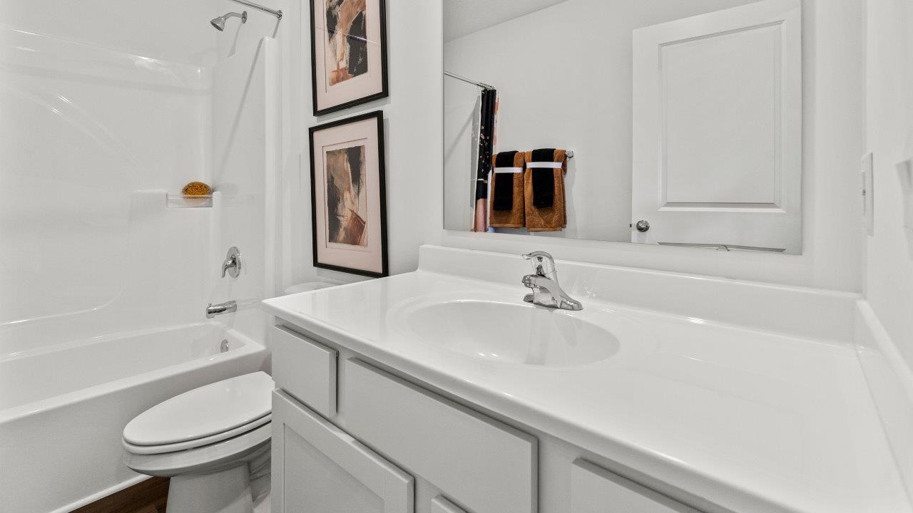 riverwalk aldridge model full bathroom with single sink vanity, fiberglass tub shower, and ryder lvp flooring